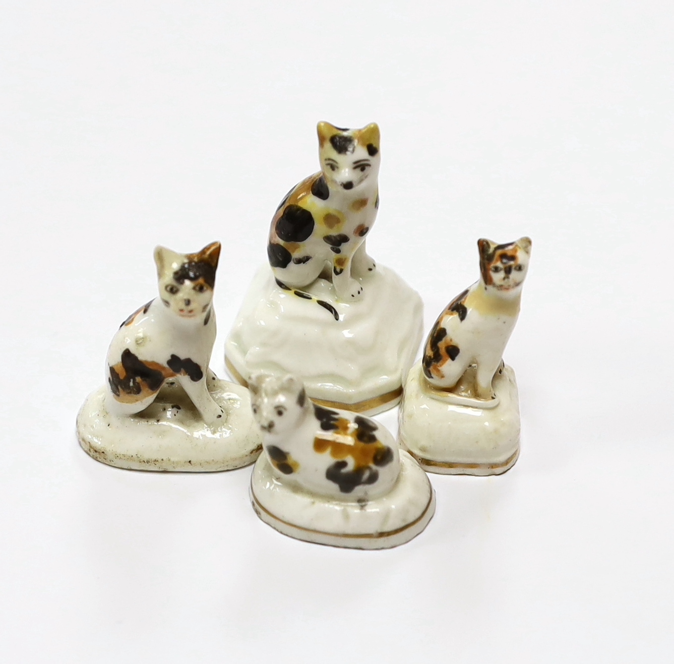 Four Staffordshire porcelain models of tortoiseshell cats, c.1830-50, three seated on shaped bases, the third model is a kitten on an oval base, tallest 5.3 cm